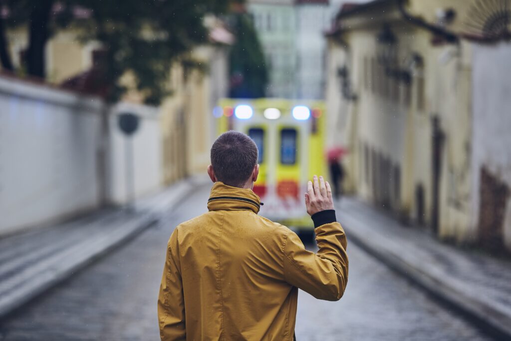 A first responder standing with a raised hand as an ambulance drives away, symbolizing the need for mental health support.