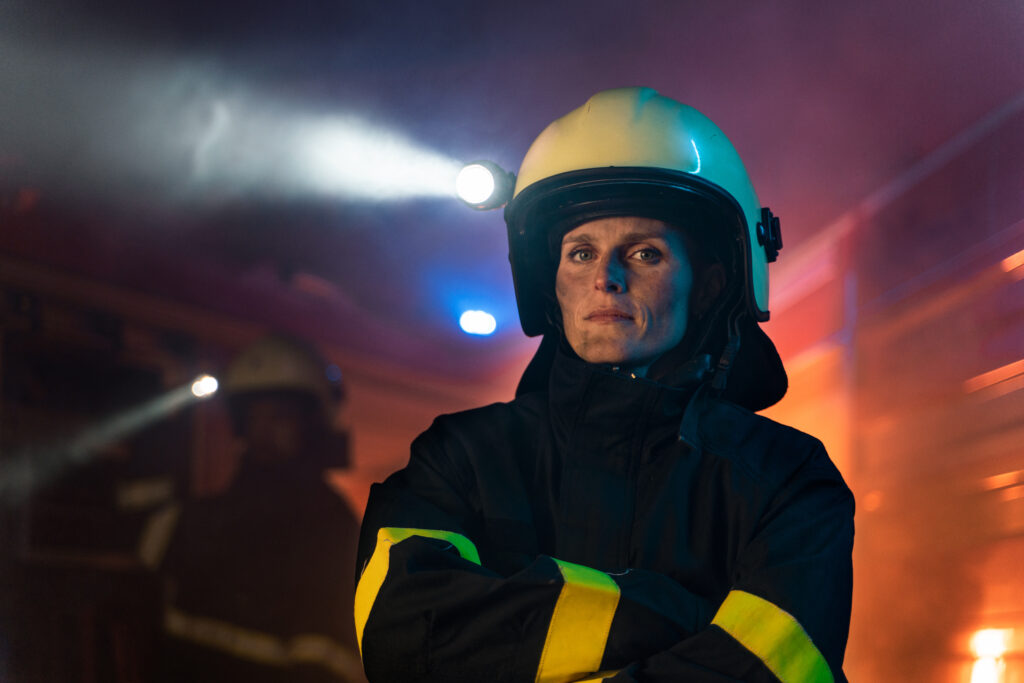 Female firefighter with her arms folded across her chest, looking serious and contemplative, representing emotional and psychological symptoms in first responders.