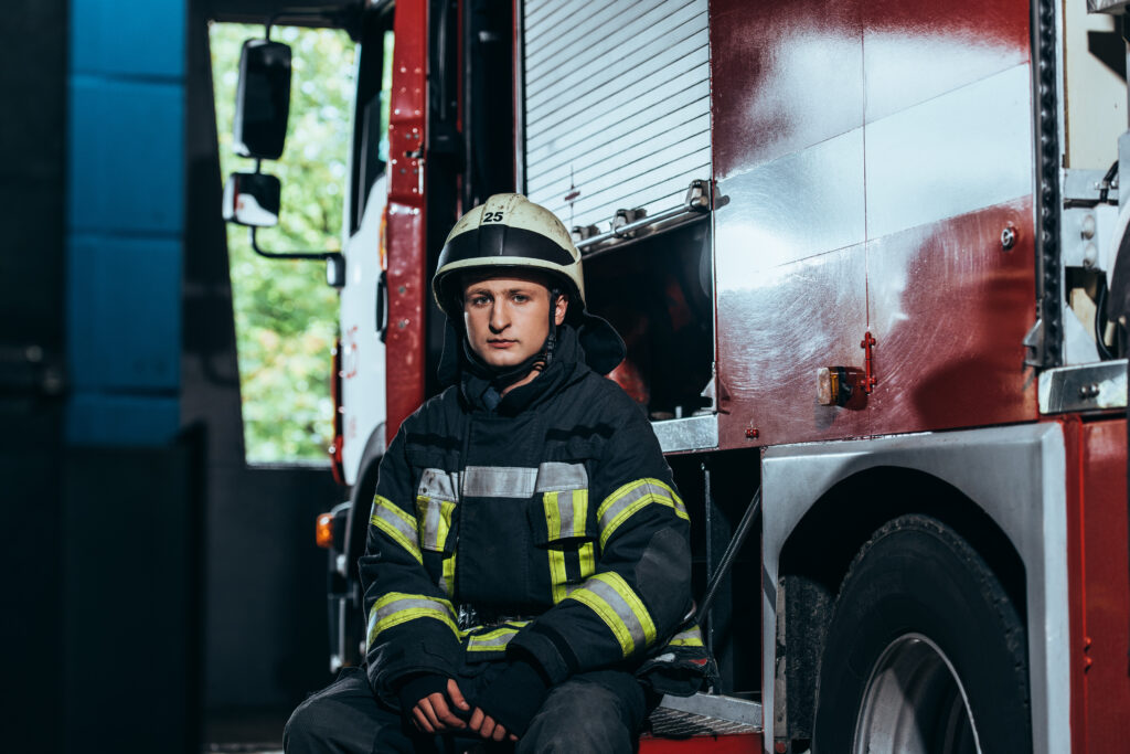 A woman firefighter in uniform stands in front of a fire station, looking very serious, illustrating the impact of organizational culture on the mental health of first responders.