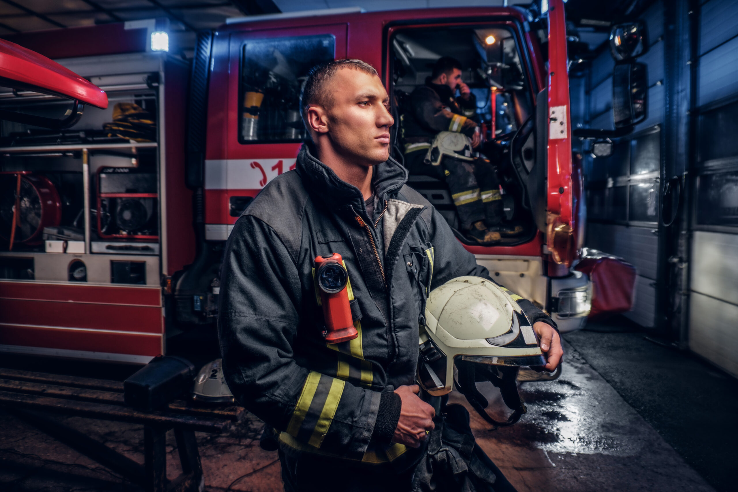 Firefighter in gear, sitting in a fire station with her helmet off, looking depressed, illustrating depression in first responders.