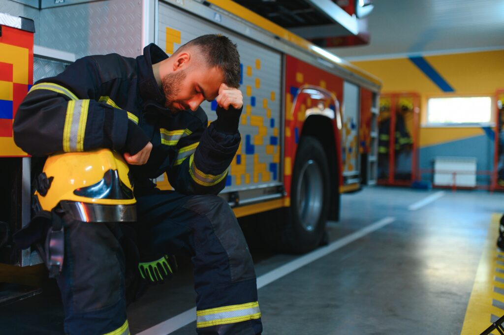 A firefighter with his head down and hand on his forehead, symbolizing the mental health struggles and the need for suicide prevention among first responders.