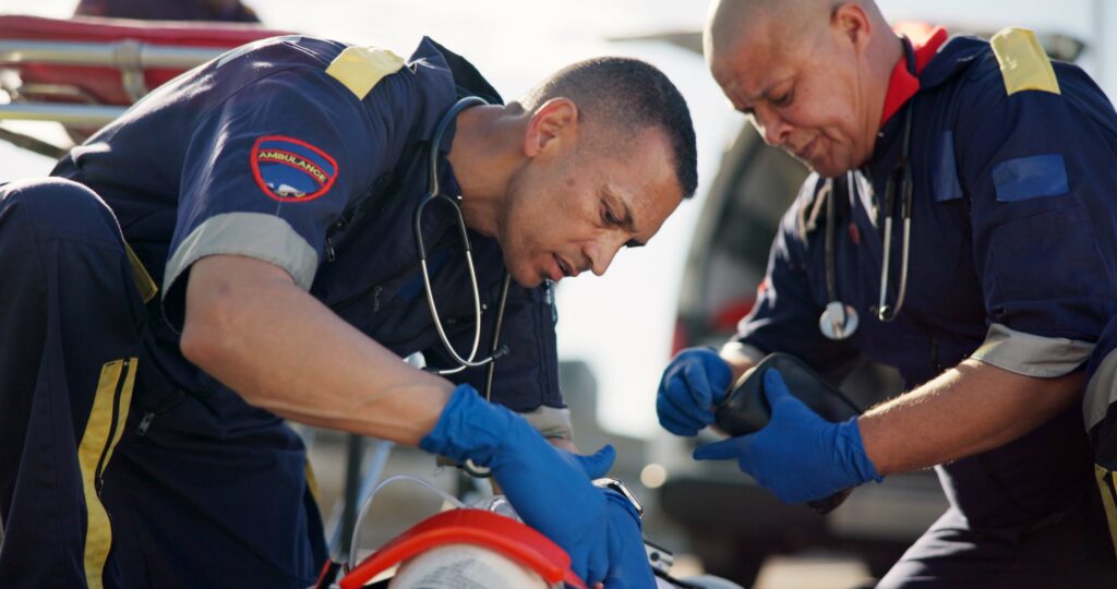 Two paramedics assisting a patient on the side of the road, highlighting the stressful environments faced by first responders and the importance of suicide prevention